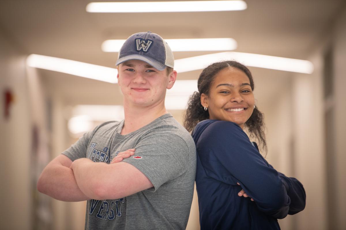 Two students back to back with arms crossed smiling.