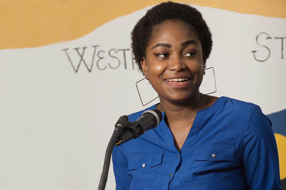 A student smiling and looking off to the side while standing in front of a microphone.