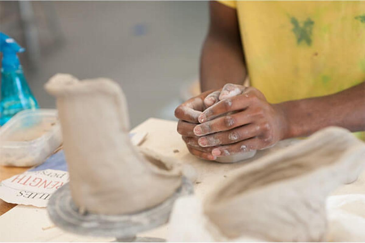 A student cups their hands next to several pieces of in-process ceramic artwork.