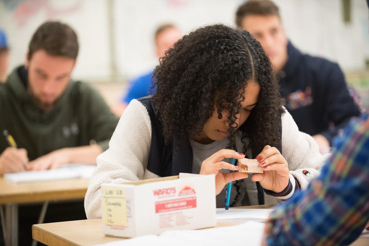 Earth System Science student looking at a rock in classroom.