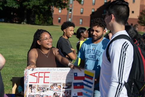 Students gathered around a "Latinx" poster, one with dark hair and glasses, one in a blue t-shirt, and another in a long, white sleeved t-shirt.