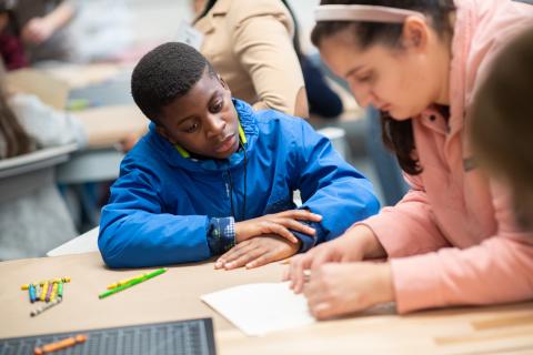 Westfield State education major and elementary school aged child sit at a desk and work together on a paper project