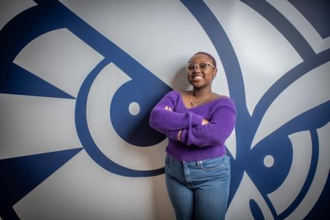 Catrina Casting, class of 2026. She is posing in front of a navy blue and white owl, and wears a purple shirt and jeans.