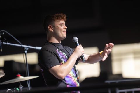 Student speaks into a microphone onstage during Westfield State’s Spring Weekend, gesturing to the audience while wearing colorful face gems.