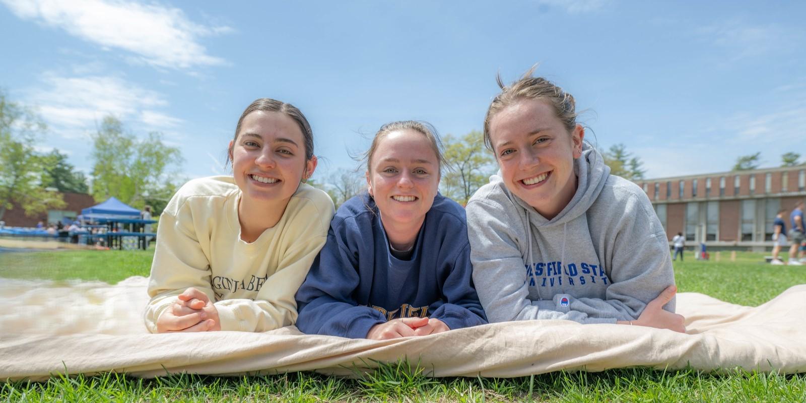 Three students lying on the campus green, smiling together.