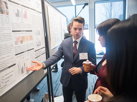 Male student in front of presentation board discussing his research during the CURCA event