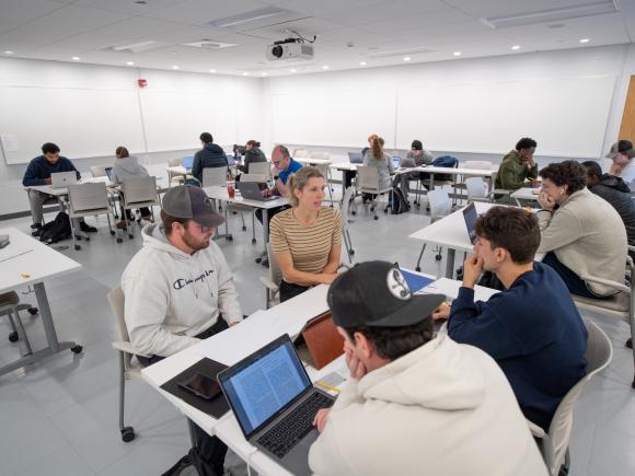 Economics class featuring instructor with small group of 3 students working on a project with laptops.