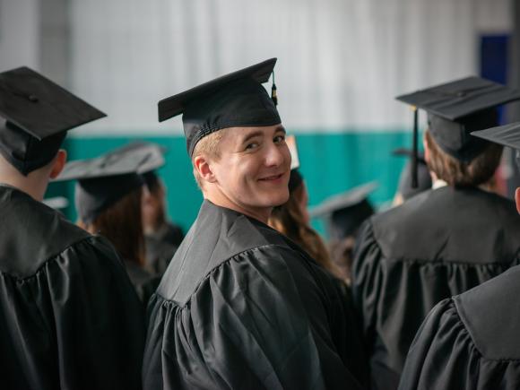 Graduate Criminal Justice Student at Commencement wearing cap and gown turned around smiling at event.