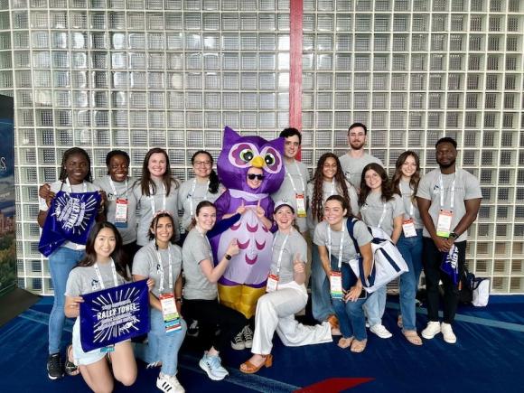 PA students at the American Academy of Physician Assistants (AAPA) National Conference in Houston, Texas. They are posing with a purple owl and hold blue signs that say 'Rally Towel'.