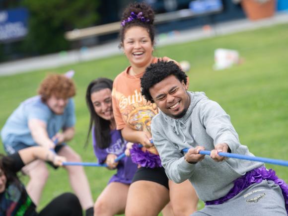 Five students play tug of war with a blue rope