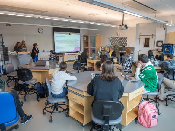 Biology classroom with students sitting at tables looking at a presentation.