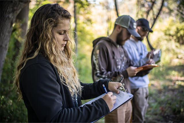 Three students making notes while standing outside in a nature area.