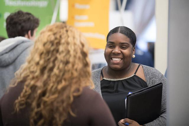 A student holding a portfolio smiles while talking to someone.