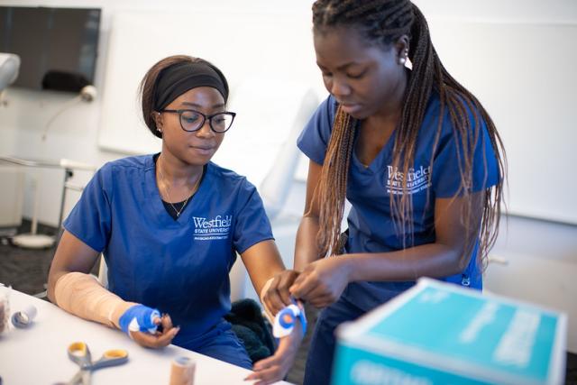 Splinting lab featuring two health science students in blue scrubs with WSU logos testing how to splint on eachother. 