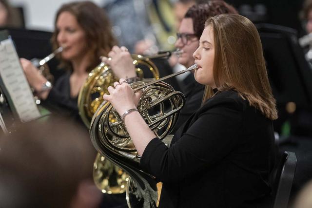 Students in the French horn section play their instruments.