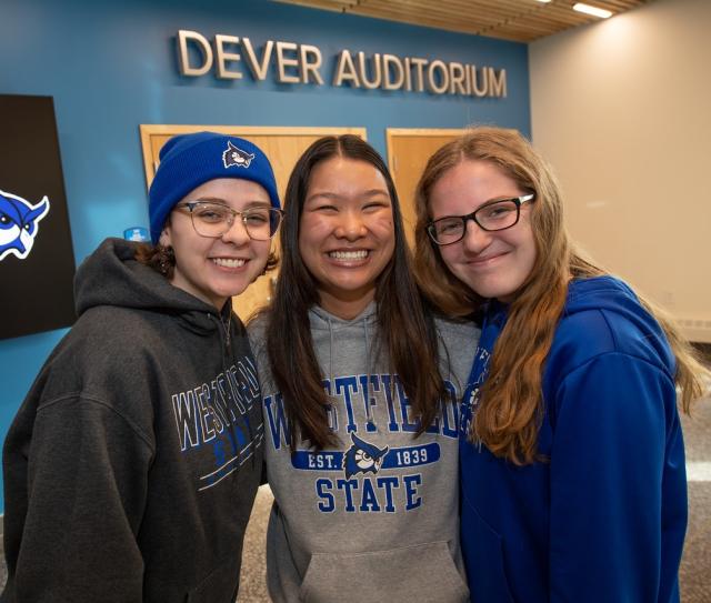 Three students smiling wearing WSU shirts in front of Dever Auditorium.