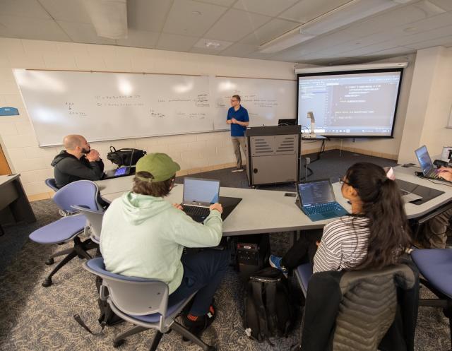  A faculty member teaching in front of students in a classroom setting.