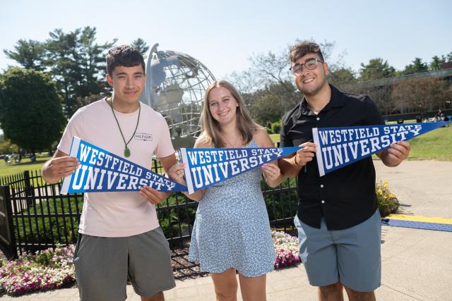 Three students smiling holding Westfield State pennant flags.