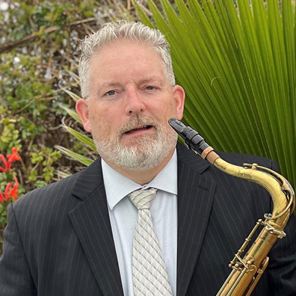 Dr. Edward Orgill stands outside while holding a saxophone.