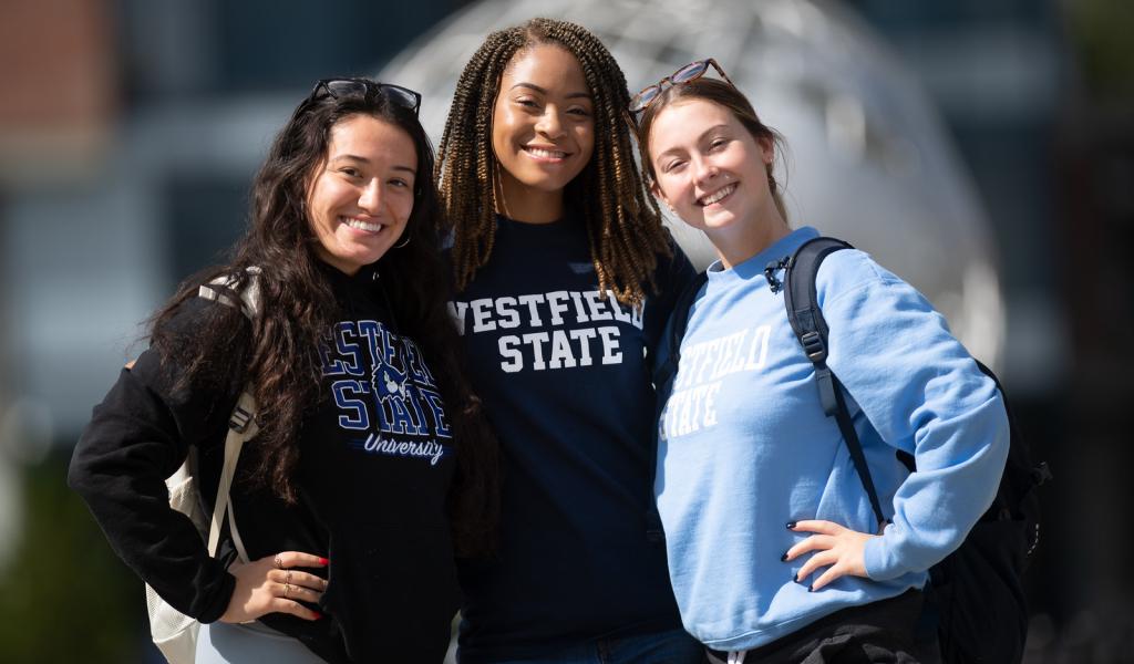 Image of three female students smiling at the camera in front of the Globe on the campus green