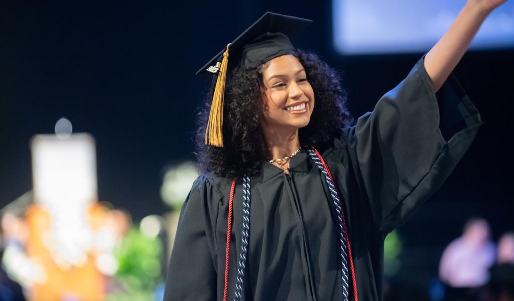 Student at commencement wearing cap and gown smiling.