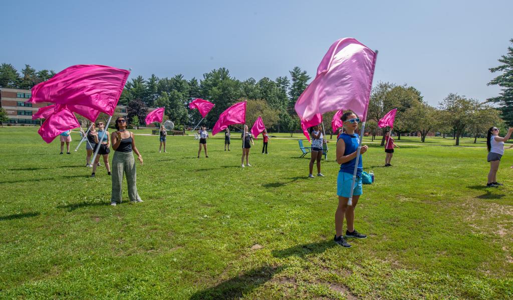 Drum Major Academy on campus green with group holding pink flags on sunny day with blue skies.