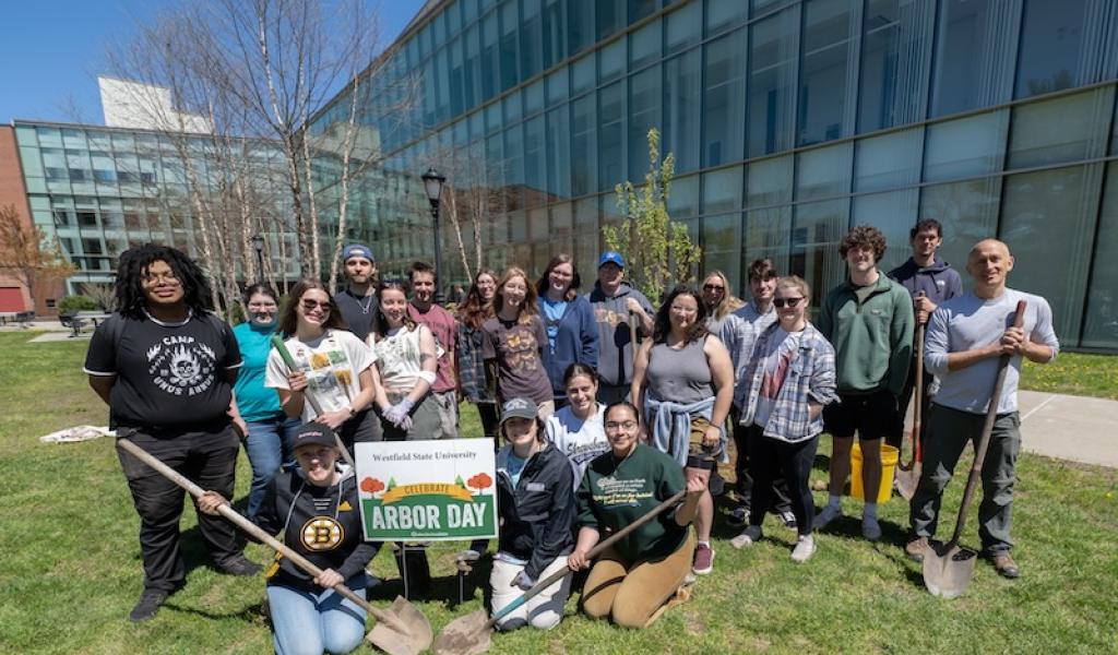 Arbor Day 2024. A group of students congregate around a white sign which says "Arbor Day" in front of the Nettie Science Building on campus. Professor Tim Parshall is with them. Two students in the front hold shovels.